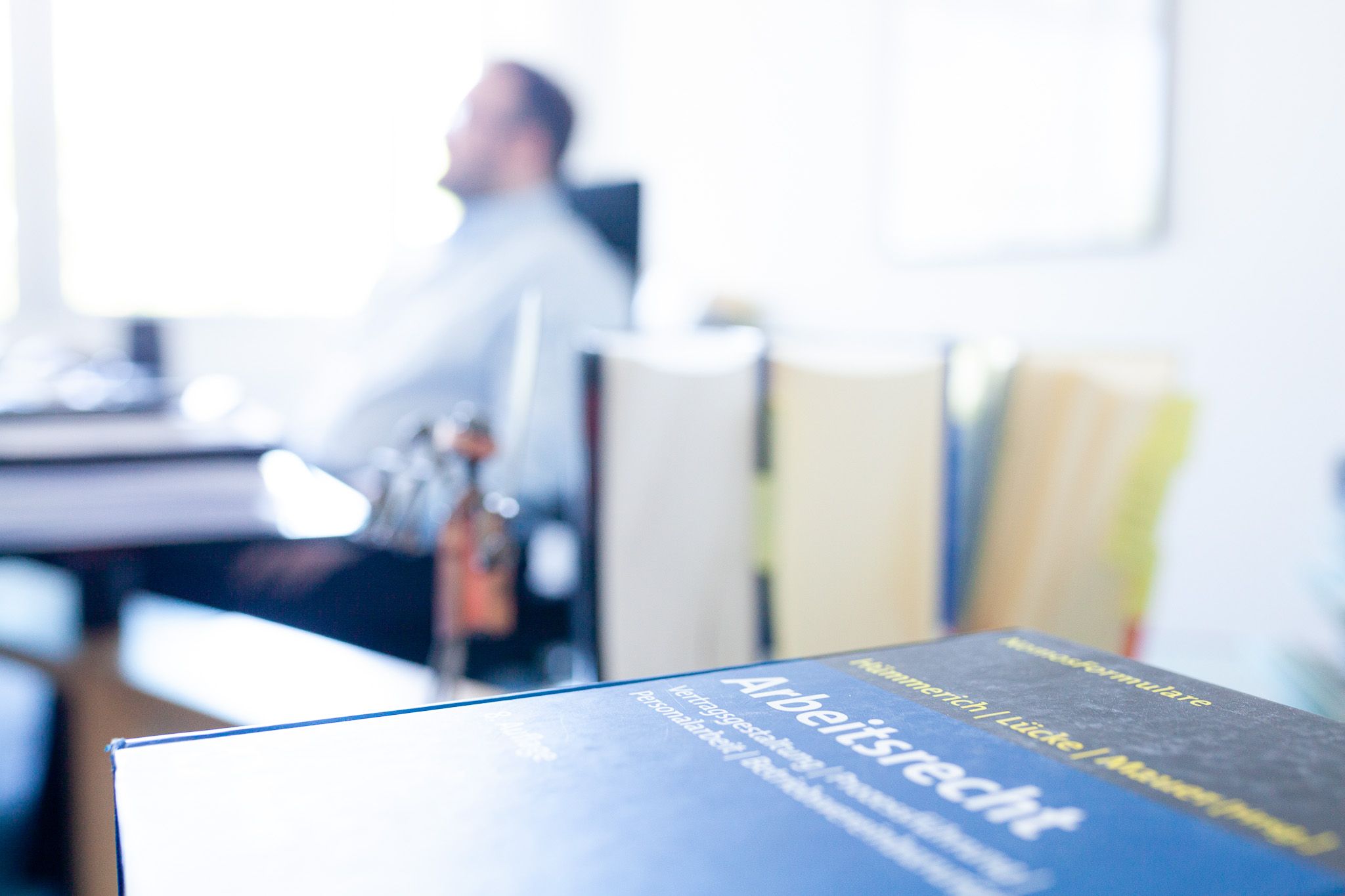 Blaues Buch "Arbeitsrecht" im Vordergrund, unscharfer Mann und Bücher im Hintergrund